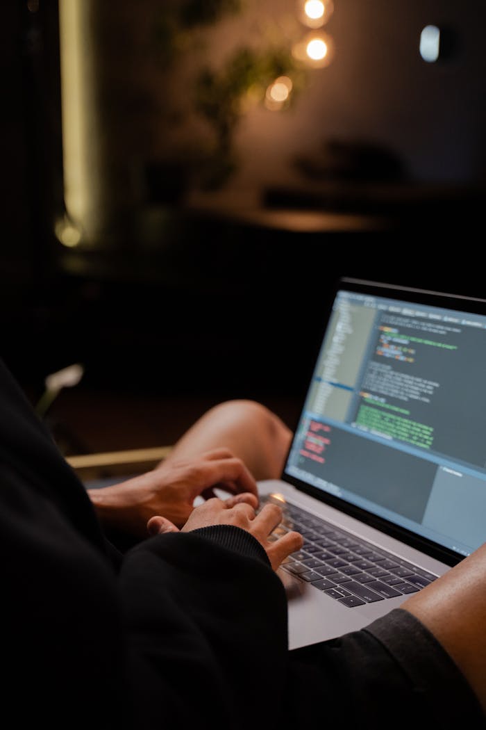 about-us Focused hands typing code on a laptop in a dimly lit room, showcasing programming activities.